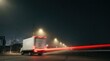 © Hryhor Denys - Delivery truck speeds past a warehouse facility during a night shift. Motion blur lights create a sense of urgent logistics and distribution.