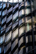 © yaqui_villegas - Curved dark glass office facade with repeating windows, showing modern architecture through reflections, geometric rhythm and abstract urban building detail