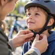 © Denis Chubchenko - Mother hands fastening safety helmet chin strap on smiling young boy outdoors before cycling. Child safety, parental care, bike helmet protection, and family recreation concept.