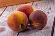 © Andrei Starostin - Three ripe peaches with yellow and red blush on weathered wooden surface, soft natural lighting, shallow depth of field