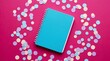 © geny - Turquoise notebook surrounded by pastel confetti on a vibrant pink background