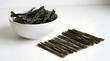© MUHAMMAD - Organic dried kombu seaweed strips in a white bowl and scattered on a minimal white surface