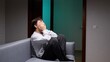 © Aliaksandr - Young man sits alone on a dim sofa, covering his face with his hands, conveying deep sadness, anxiety and isolation in a quiet, somber indoor scene
