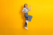 © deagreez - Cheerful young woman in fashionable casual attire jumping with joy on yellow background showcasing vibrant lifestyle