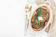 © FuzullHanum - Raw ribeye steak in ceramic baking dish with herbs, spices, cutlery and napkin on white plaster
