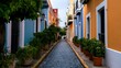 © Wuttichai - A narrow cobblestone street lined with colorful buildings and potted plants under a clear sky