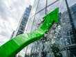 © Xisxas - A vibrant green business arrow shatters through the glass facade of a towering skyscraper showcasing immense financial momentum breakthrough and corporate ambition during daytime operations