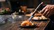 © TaZJunG - Professional chef using a kitchen blowtorch to sear fresh salmon sushi nigiri.