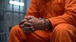 © Tommy Studio - Close-up of a prisoner in an orange jumpsuit sitting with handcuffed hands inside a jail cell
