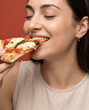 © Rendara Studio - Indulgent woman bites a cheesy pizza slice, with a smile in an intimate close crop