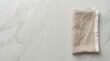 © BZXO - Minimalist top down view of a folded beige linen napkin on a light gray marble table surface with copy space.