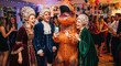 © ArtExpert - Humorous stock photo of eccentric friends celebrating a party in historical costumes and an inflatable dinosaur suit while looking at a smartphone.