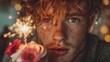© rahit - Young man with red hair and freckles holding a birthday cupcake with a lit sparkler in a dimly lit room with bokeh lights
