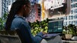 © DC Studio - Black woman analyzes investment statistics and charts on a laptop while sitting on a park bench, working remotely outdoors and reading financial data from a dashboard interface to solve tasks.
