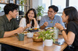 © Maswa - Happy Asian colleagues enjoying a friendly lunch together, talking and laughing around a wooden table in a modern office breakroom