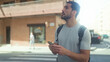 © Krakenimages.com - Man holding smartphone with both hands, scrolling and glancing up while standing on a street crosswalk by a storefront; contemplation navigation.