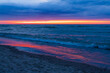 © Nadiia - Pink Sunset Reflection Across Dark Ocean and Sandy Beach. A narrow pink and orange sunset glows along the horizon above a deep blue ocean. The warm colors are reflected across the wet sandy beach