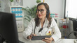 © Krakenimages.com - Woman doctor in white coat with stethoscope and headset writing on a tablet while viewing a computer screen in a clinic building; calm focus.