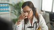 © Krakenimages.com - Woman doctor with stethoscope pinches nose bridge and wears headset while seated at desk in medical building; compassion fatigue.