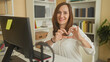 © Krakenimages.com - Woman at computer typing and shaping hands into a heart gesture in an office building; warmth connection.