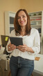 © Krakenimages.com - Woman holding tablet with hands visible, smiling while reading screen, leaning on desk in an office area inside a building; confidence productivity.