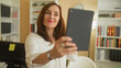 © Krakenimages.com - Woman holds tablet at arm's length for a selfie in an office inside a building; contentment connection.