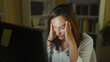 © Krakenimages.com - Woman rubbing temples at computer in home office, leaning forward with hands on temples and tired expression; stress fatigue.