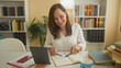 © Krakenimages.com - Woman writing with a pen in a notebook at a desk with tablet, coffee and books in an office building; focus productivity.