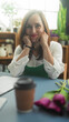 © Krakenimages.com - Woman florist with hands cupping cheeks, smiling over purple tulips and takeaway coffee on table in studio; contentment.