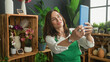 © Krakenimages.com - Woman florist in green apron holds tablet up with both hands taking selfie inside building; small business pride.