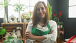 © Krakenimages.com - Woman florist in green apron smiling with crossed arms among vases and plants by a sunlit window in studio; confidence.