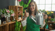 © Krakenimages.com - Woman florist holding a metal watering can and showing thumbs up in studio surrounded by flowers and wooden shelves; confidence care.