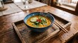 © emran - Bowl of steaming spicy curry soup garnished with lime and herbs on wooden tray for warm meal and authentic dining experience.