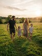 © bp - Happy Family Walking Together Through Green Meadow During Golden Hour Sunset With Warm Backlighting