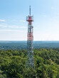 © Amazing Aerial - Aerial view of Muggelberge Antenne radio antenna rising above the dense green forest canopy under a clear blue sky Berlin, Berlin, Germany.