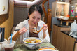 © leungchopan - Woman eating delicious beef noodle soup in restaurant with spoon