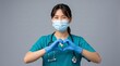© mikopuccino - Asian female healthcare worker in teal scrubs and face mask forming a heart gesture with gloved hands