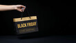 © Iren - Woman hand holding black and gold paper shopping bag with Black Friday text isolated on dark background retail sale concept.