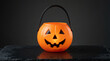 © Riverruno - Bright orange plastic pumpkin candy bucket for trick or treat on a dark slate background