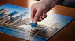 © Alla - hand placing final puzzle piece into a completed urban skyline jigsaw featuring modern cityscape along a waterfront, 3d