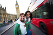 © CarlosBarquero - Joyful interracial couple having fun in London, with Big Ben and a red double decker bus behind. Playful piggyback pose, wide angle travel portrait that radiates energy and spontaneity.