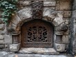 © Alexei - Ornate iron grate set in a weathered stone arched wall with carved relief and ivy foliage, historic masonry entrance architectural detail
