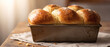 © SIMANG - A freshly baked golden-brown brioche loaf sits in a metal baking pan, with a glossy, sugared crust, placed on a linen cloth over a wooden table.