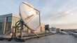 © Mia - Large metallic satellite dish antenna installed on building rooftop against sky representing telecommunication and data transmission technology