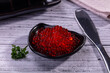 © Andrei Starostin - Red caviar in black bowl on rustic wooden table with parsley and knife