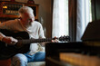 © Rob and Julia Campbell/Stocksy - Older man playing acoustic guitar at home by a window