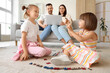 © Pixel-Shot - Family work-life balance and remote work, parents using laptop on sofa while children play with alphabet letters on living room floor at home