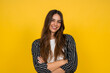 © Daniel - Smiling young woman with long hair and crossed arms poses confidently against a vibrant yellow background, conveying happiness, approachability and modern casual style for lifestyle, business casual