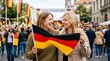 © Len_mik - Two happy women holding German flag at outdoor festival. Friends celebrating German Unity Day in city street. Public holiday event