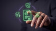 © SYATRI RAWU - Close-up of a businessman's hand interacting with glowing green neon icons representing environmental sustainability and green energy renewable goals.